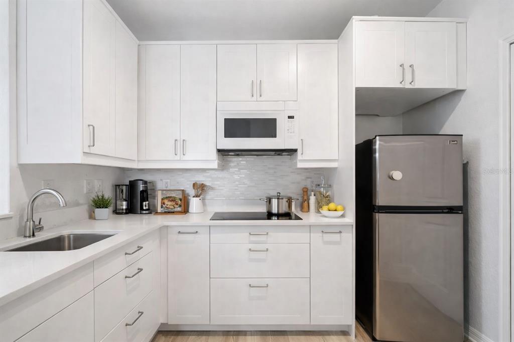 A modern kitchen features white cabinetry, a stainless steel refrigerator, and a light-colored backsplash — 8824 DUNES COURT COURT UNIT 103, KISSIMMEE, FL