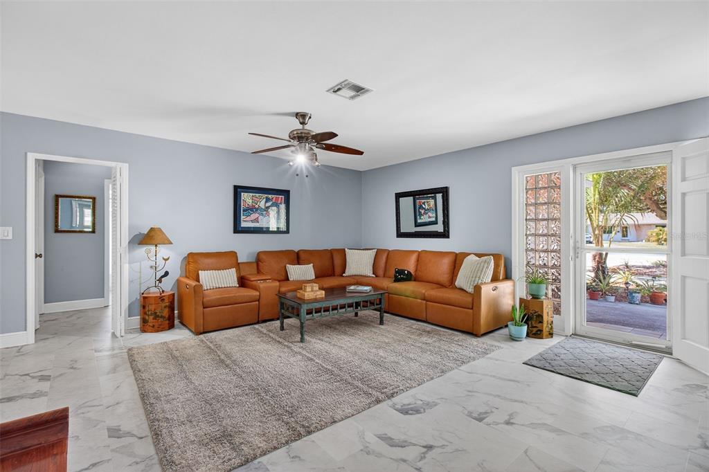 A living room features a tan leather sectional, a gray area rug, and marble flooring — 5723 1ST STREET NE, ST PETERSBURG, FL