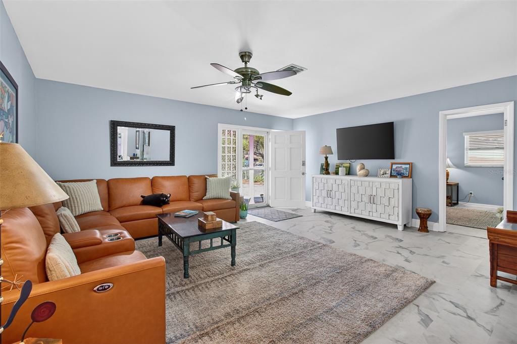 A living room with a leather sectional, area rug, white media console, and tile flooring — 5723 1ST STREET NE, ST PETERSBURG, FL