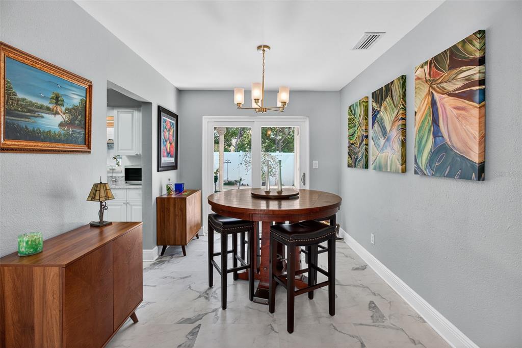 A dining room features a round wooden table, bar stools, and artwork on gray walls — 5723 1ST STREET NE, ST PETERSBURG, FL