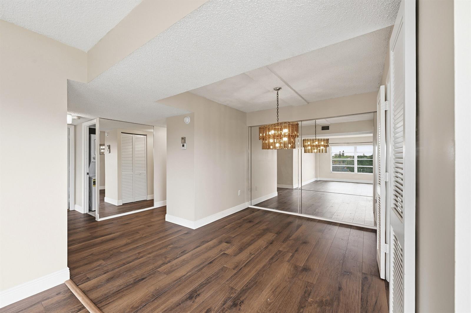 An empty room with wood-look flooring, mirrored closet doors, and a decorative chandelier — 4158 Inverrary Drive # 511, Lauderhill FL 33319, LAUDERHILL, FL