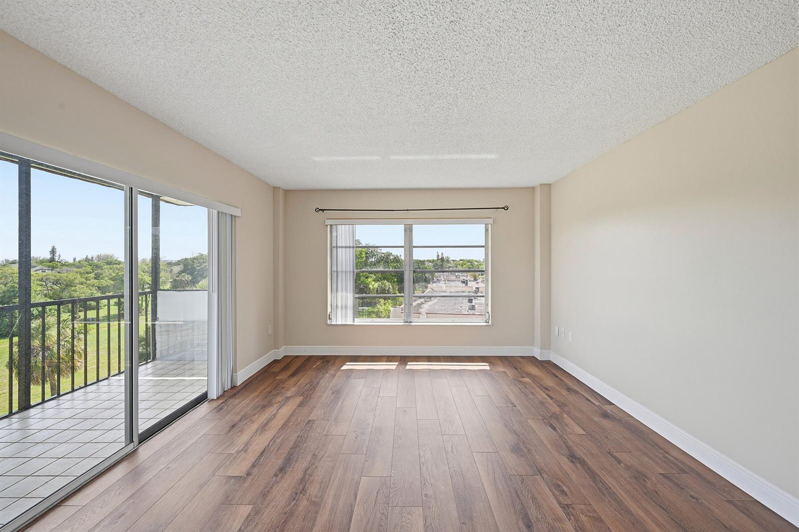 An empty room features wood-look flooring, a sliding glass door to a balcony, and a window — 4158 Inverrary Drive # 511, Lauderhill FL 33319, LAUDERHILL, FL
