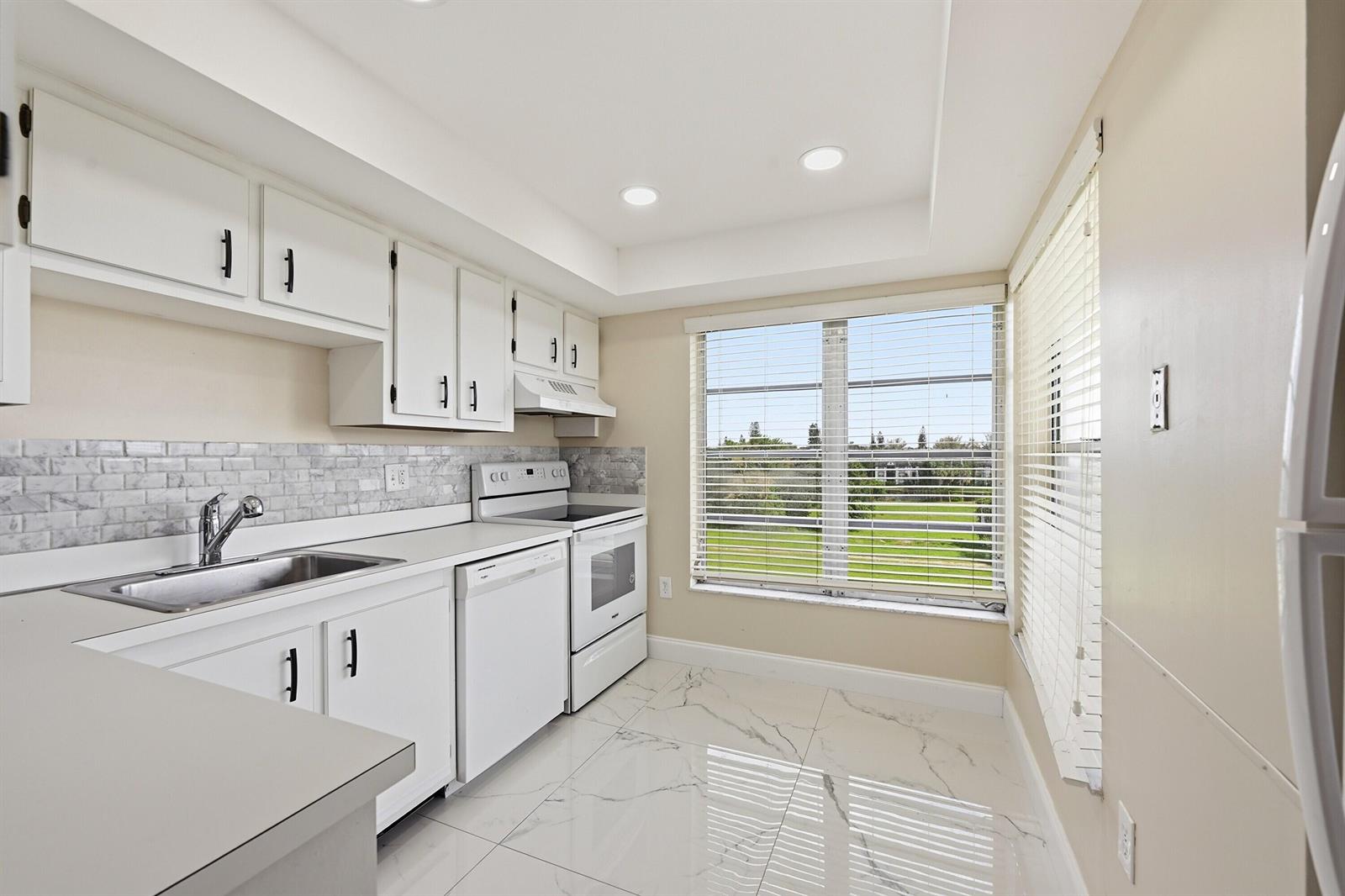 A kitchen with white cabinets, stainless steel sink, white appliances, and marble-look tile flooring — 4158 Inverrary Drive # 511, Lauderhill FL 33319, LAUDERHILL, FL