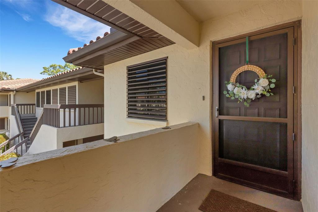 An exterior view of a covered apartment entryway with a screen door and a wreath — 5252 LAKE VILLAGE DRIVE UNIT 54, SARASOTA, FL