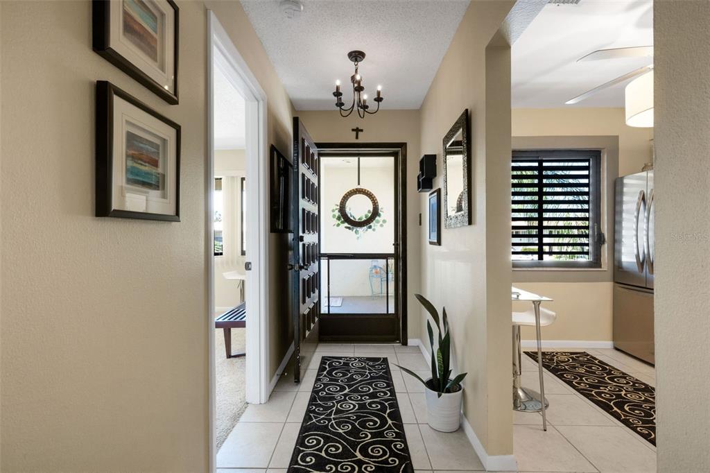 A tiled entryway features a black runner rug, a chandelier, and a glass-paneled front door — 5252 LAKE VILLAGE DRIVE UNIT 54, SARASOTA, FL