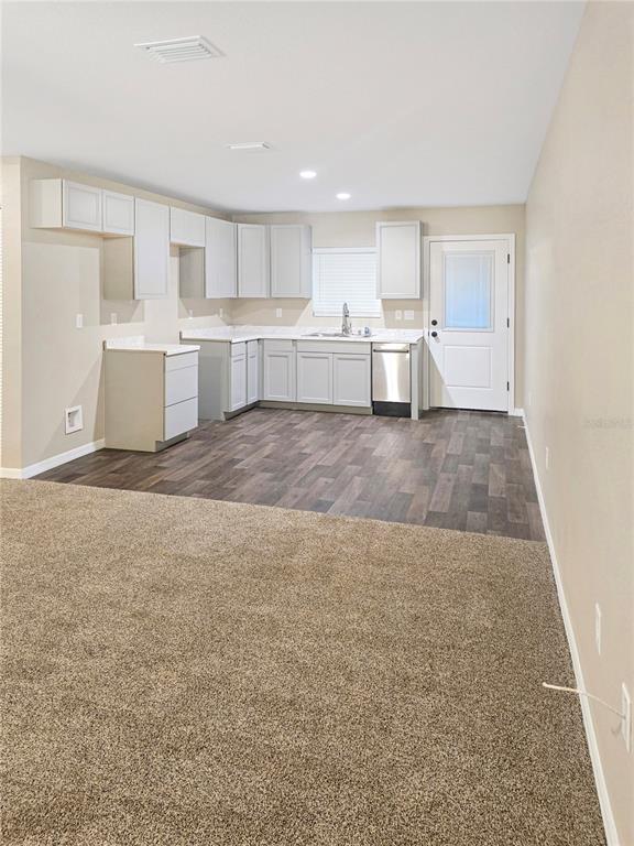 A kitchen with light gray cabinets and dark wood-look flooring opens to a carpeted area — 19920 SW 108TH PLACE, DUNNELLON, FL