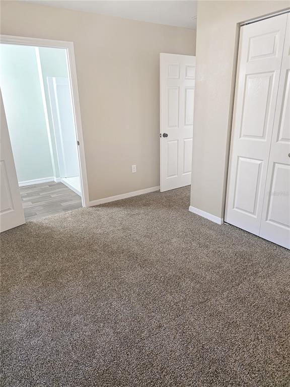 A carpeted bedroom features a closet with white doors and an open doorway to a bathroom — 19920 SW 108TH PLACE, DUNNELLON, FL