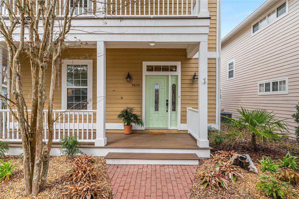 A light green front door with a side light sits on a covered wooden porch — 5034 NW 11TH PLACE, GAINESVILLE, FL