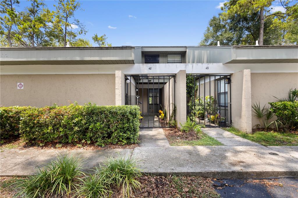 The exterior view shows two adjacent residential units with gated entryways and a shared hedge — 7200 SW 8TH AVENUE UNIT H48, GAINESVILLE, FL