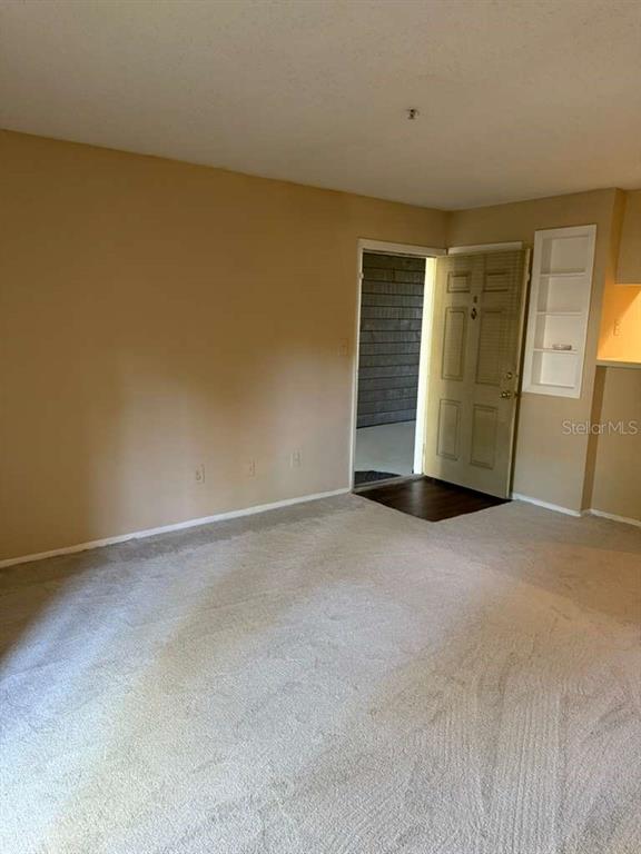 A carpeted living room features a beige wall, a doorway, and built-in wall shelving — 199 AFTON SQUARE UNIT 103, ALTAMONTE SPRINGS, FL