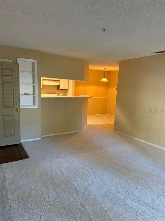 A living room with beige carpet leads to a kitchen breakfast bar and dining area — 199 AFTON SQUARE UNIT 103, ALTAMONTE SPRINGS, FL