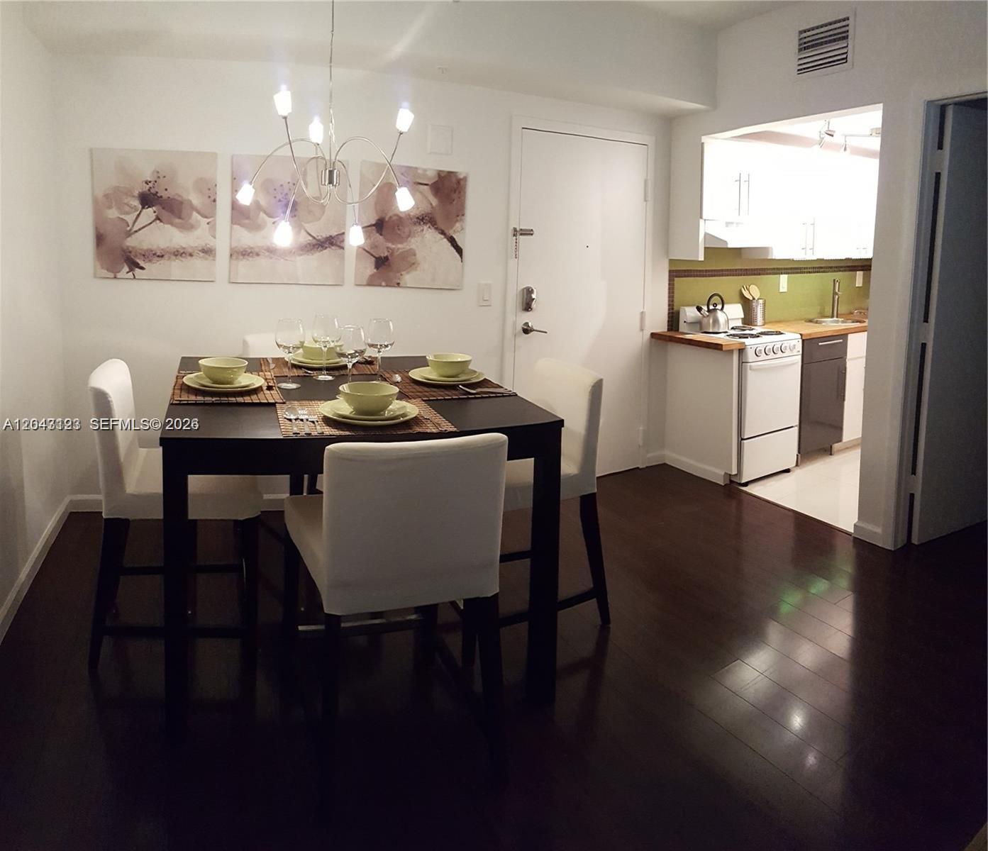 A dining area with a dark table and white chairs sits adjacent to a kitchen — 1550 Drexel Ave # 106, Miami Beach FL 33139, MIAMI BEACH, FL