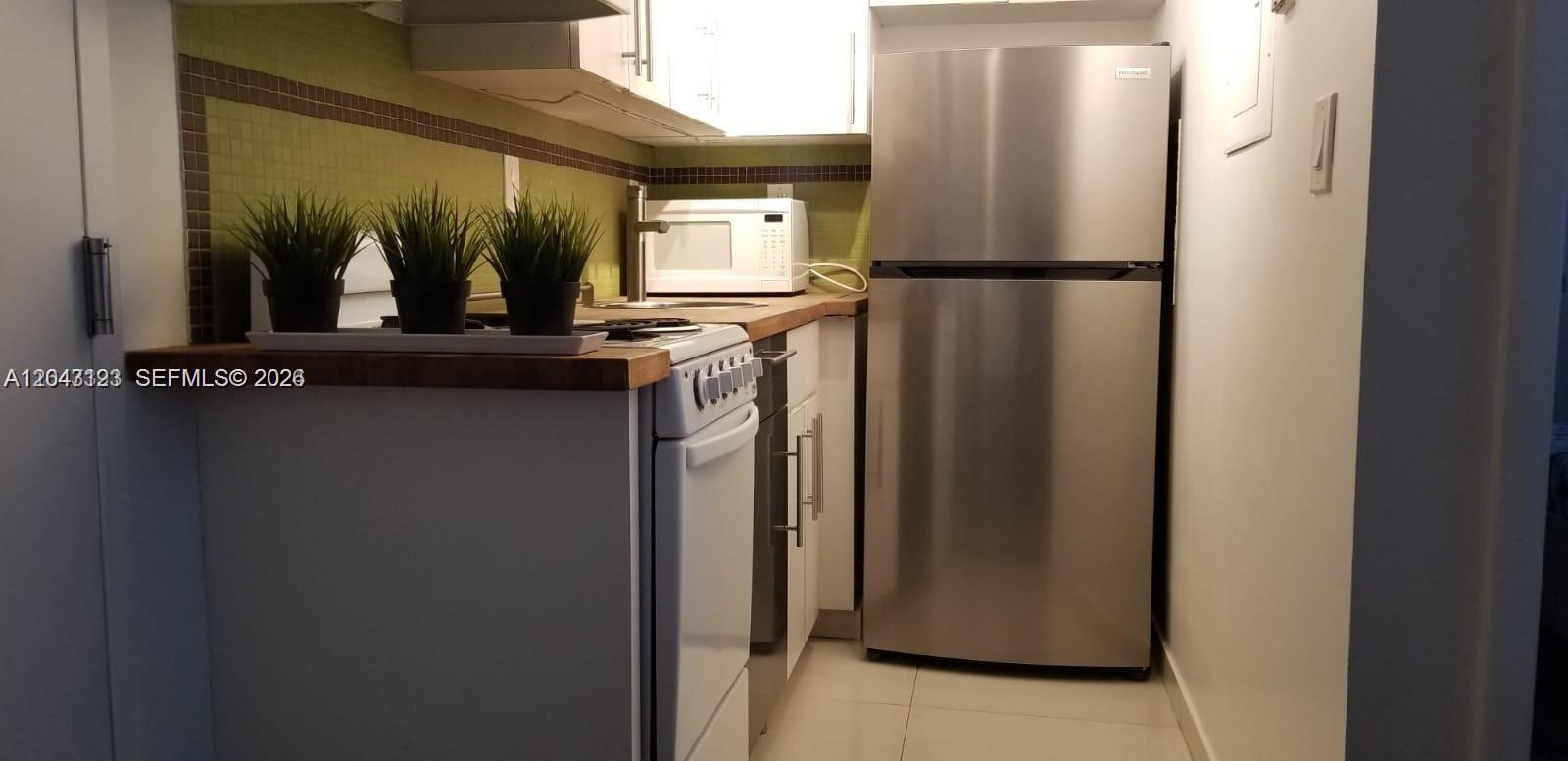 A small kitchen features white cabinets, stainless steel appliances, and a green tiled backsplash — 1550 Drexel Ave # 106, Miami Beach FL 33139, MIAMI BEACH, FL