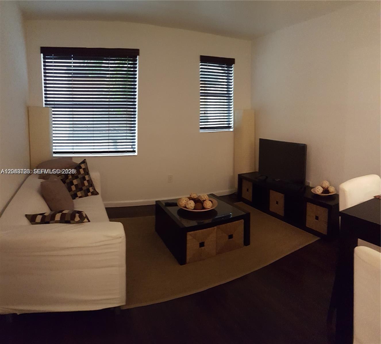 A living room features a white sofa, a black coffee table, and a television stand — 1550 Drexel Ave # 106, Miami Beach FL 33139, MIAMI BEACH, FL