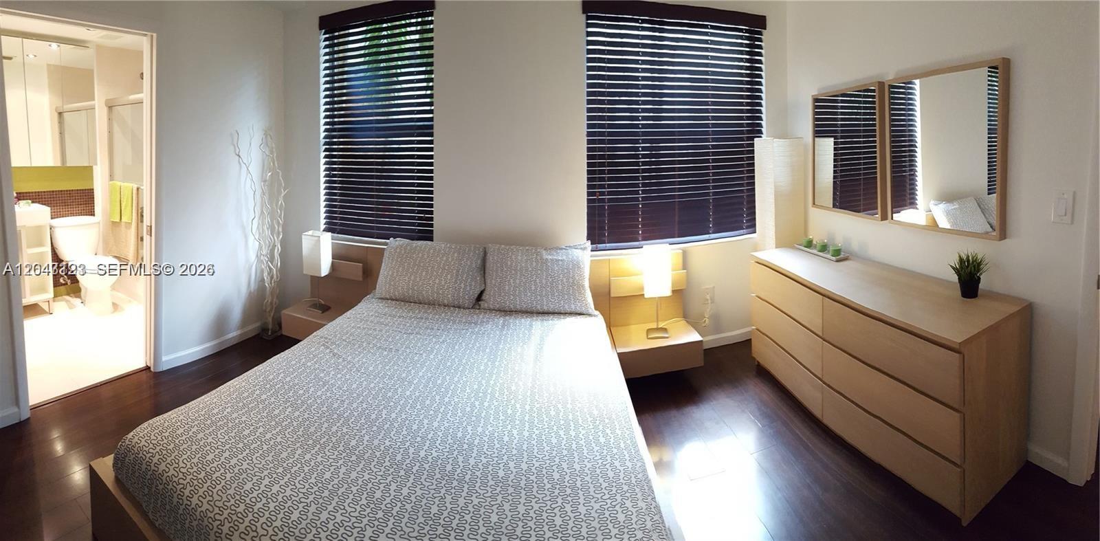 A bedroom features a bed, two floating nightstands, a dresser with mirrors, and an attached bathroom — 1550 Drexel Ave # 106, Miami Beach FL 33139, MIAMI BEACH, FL