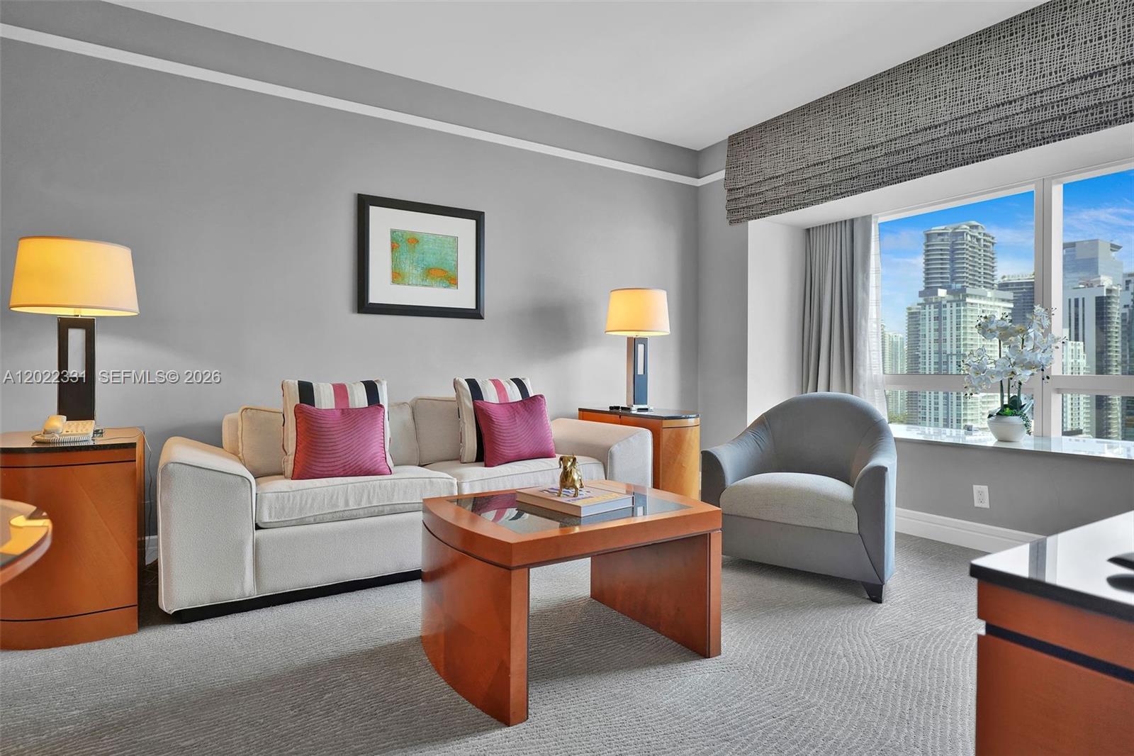 A living room features a beige sofa, a grey armchair, and a view of city buildings — 1435 Brickell Ave # 3210, Miami FL 33131, MIAMI, FL