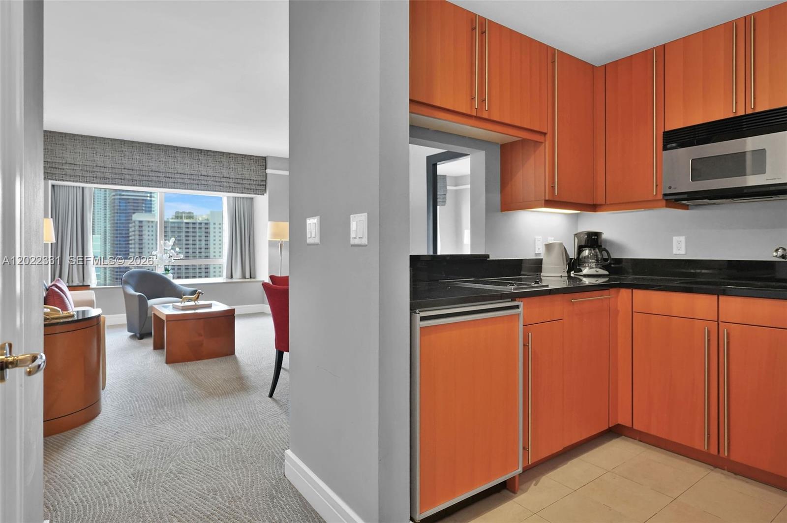 A kitchen with wood cabinets and black countertops overlooks a living area with city views — 1435 Brickell Ave # 3210, Miami FL 33131, MIAMI, FL