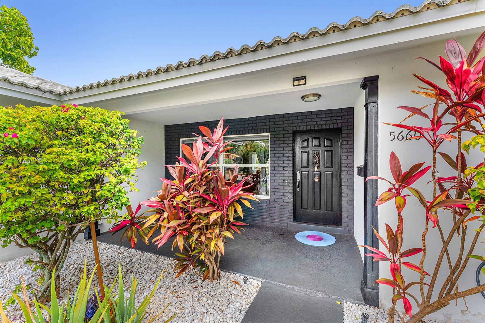 The exterior entrance features a black brick wall, a dark front door, and tropical plants — 5660 Nassau Drive, Boca Raton FL 33487, BOCA RATON, FL