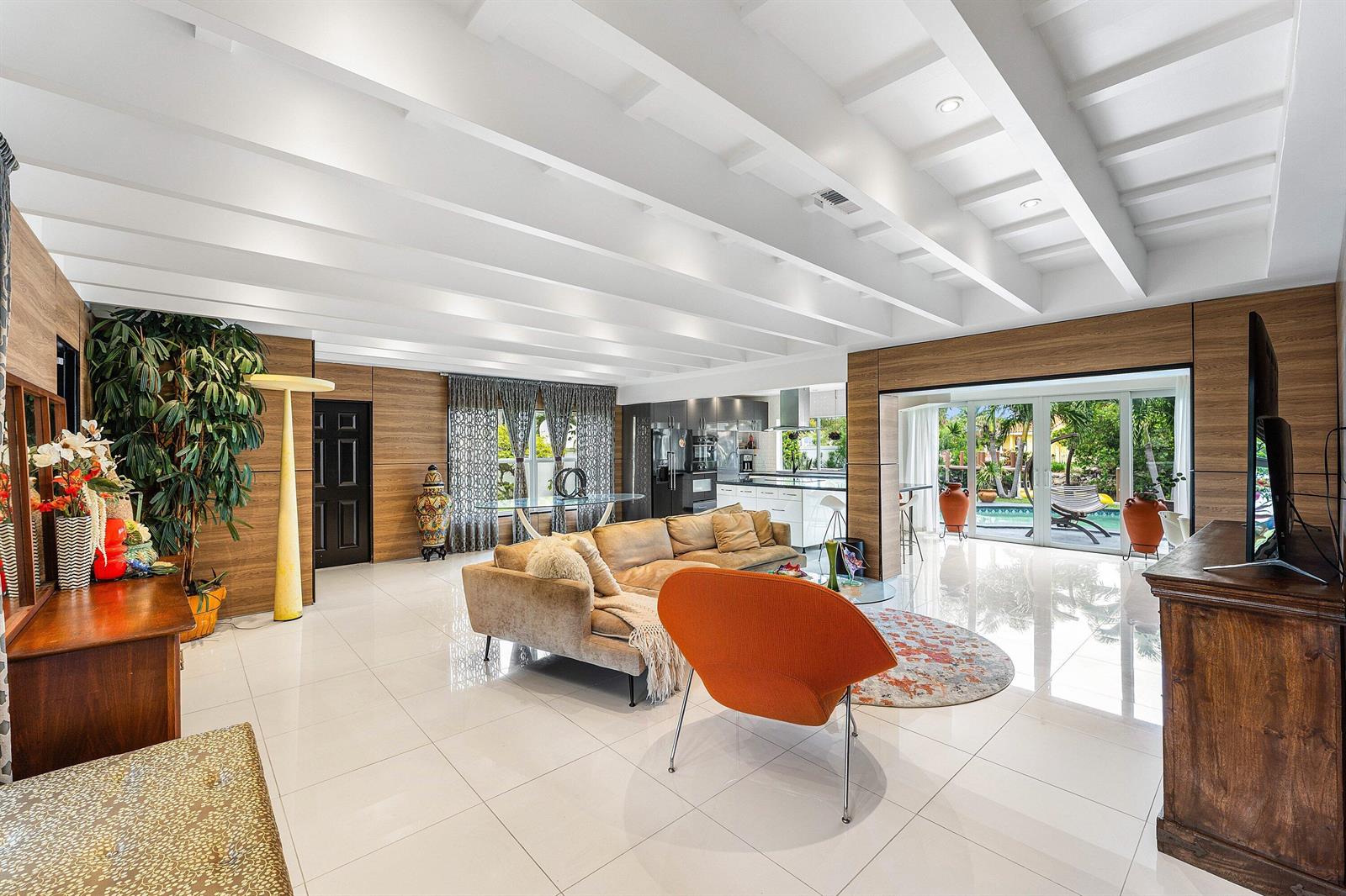 A modern living room with wood-paneled walls, white tile floors, and a view of a pool — 5660 Nassau Drive, Boca Raton FL 33487, BOCA RATON, FL