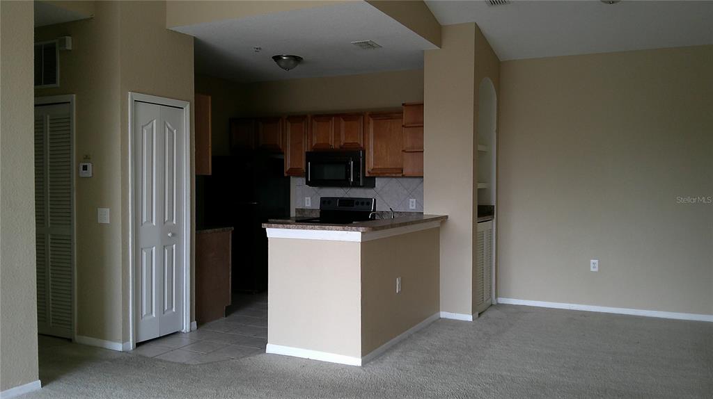 A kitchen with wooden cabinets and a breakfast bar overlooks a carpeted living area — 6141 METROWEST BOULEVARD UNIT 308, ORLANDO, FL