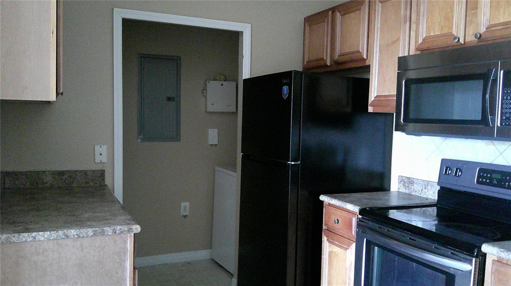 A kitchen features wood cabinets, a black refrigerator, a microwave, and a stove — 6141 METROWEST BOULEVARD UNIT 308, ORLANDO, FL