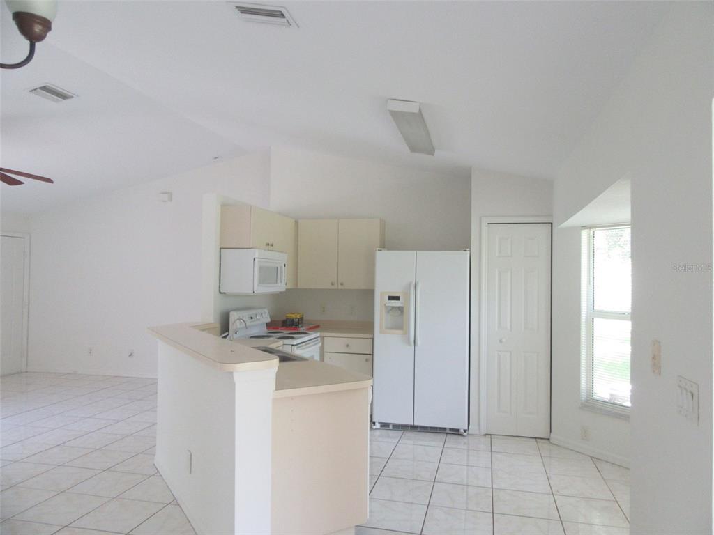 A kitchen with white cabinets, white appliances, and tiled floors opens to a living area — 2716 VOGLER LANE, NORTH PORT, FL