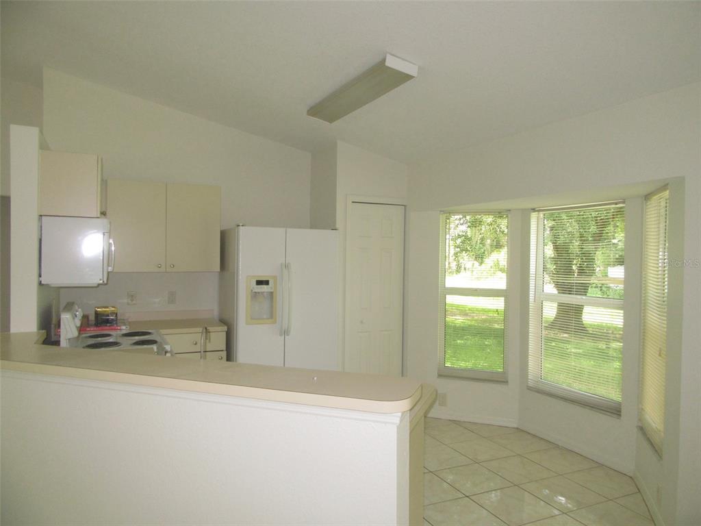 A kitchen with white appliances and cabinets overlooks a tiled dining area with large windows — 2716 VOGLER LANE, NORTH PORT, FL