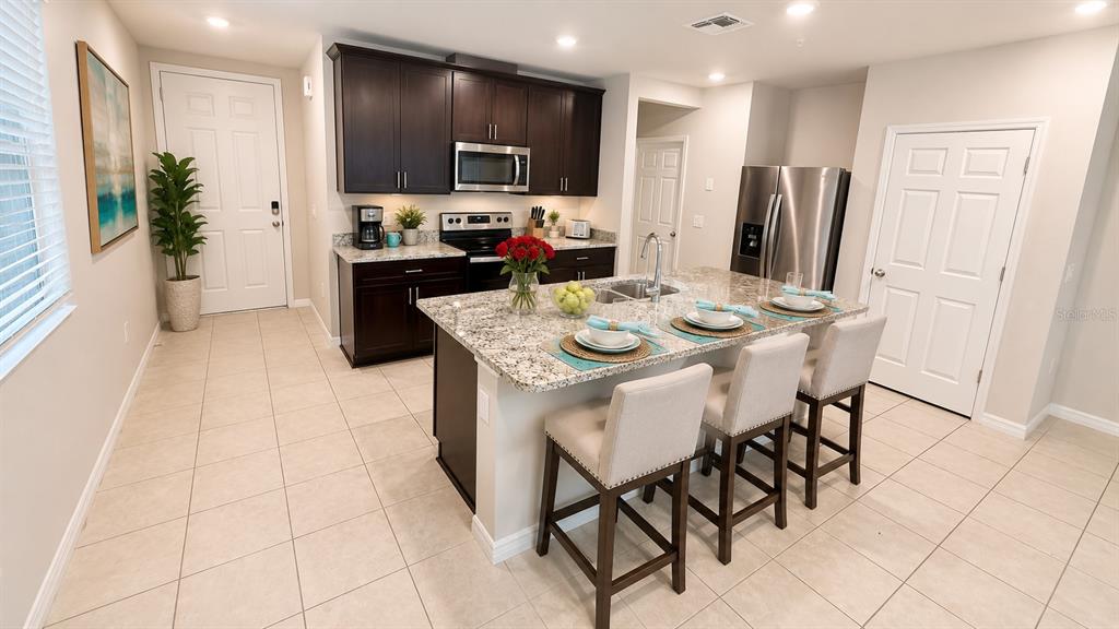 A kitchen features dark wood cabinets, granite countertops, a center island, and three bar stools — 2463 SWEET VIBURNUM WAY, OCOEE, FL
