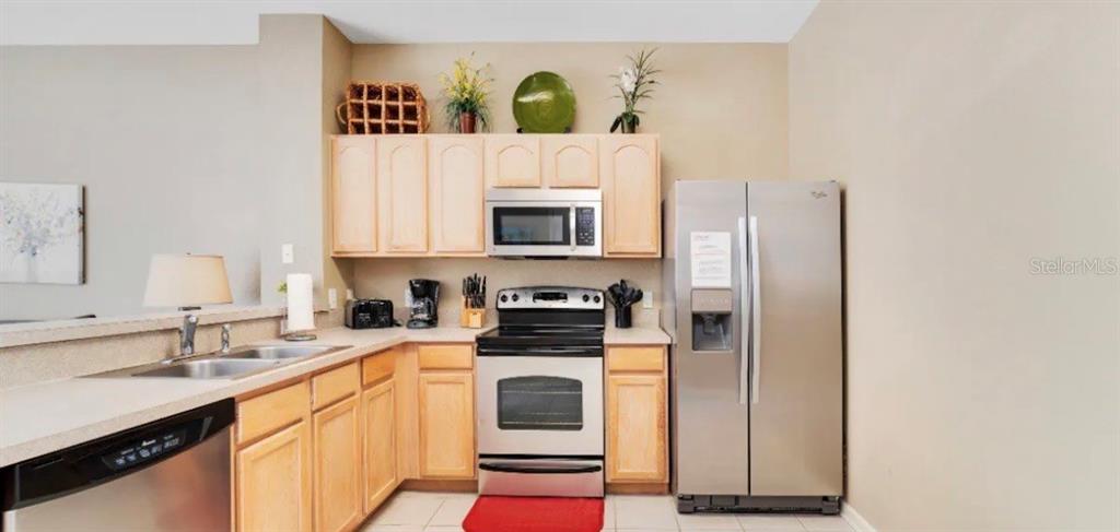 A kitchen features light wood cabinets, stainless steel appliances, and a double basin sink — 7663 SIR KAUFMANN COURT, KISSIMMEE, FL