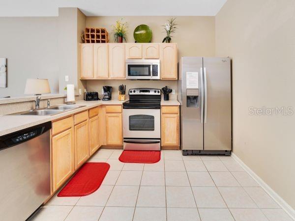 A kitchen with light wood cabinets, stainless steel appliances, and beige tile flooring — 7663 SIR KAUFMANN COURT, KISSIMMEE, FL