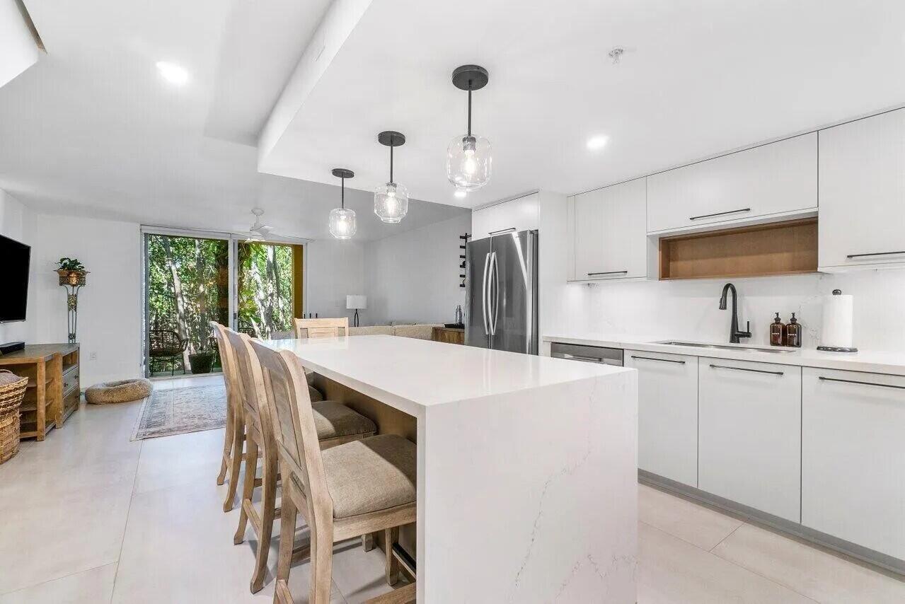 A modern white kitchen features a large quartz island with bar seating and pendant lighting — 1100 Scotia Drive # 105, Hypoluxo FL 33462, HYPOLUXO, FL