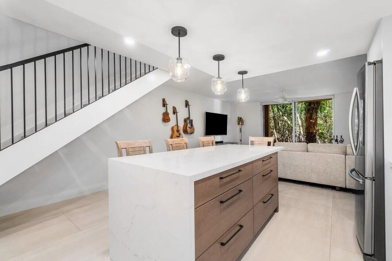 A kitchen island with wood cabinets and a white countertop sits before a living area — 1100 Scotia Drive # 105, Hypoluxo FL 33462, HYPOLUXO, FL