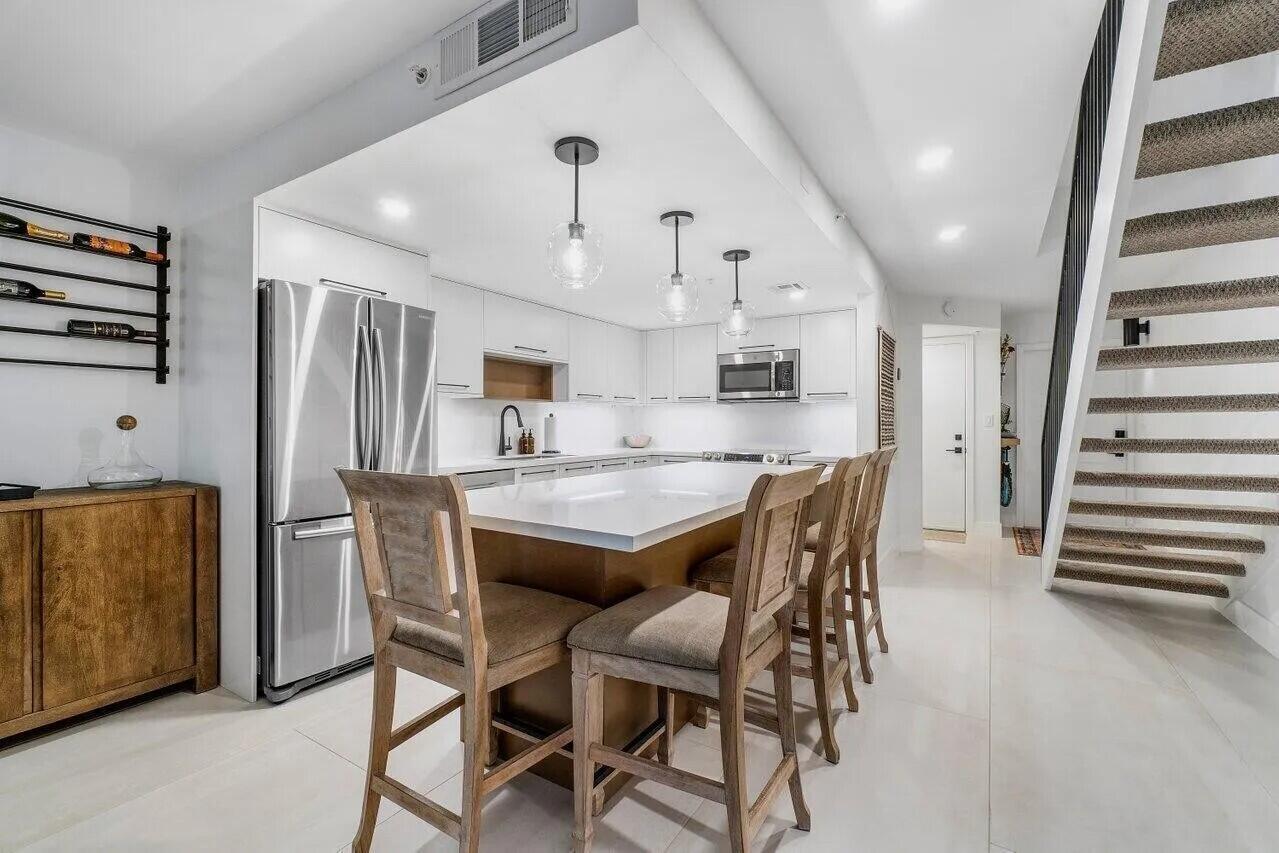 A modern kitchen features a white island with bar stools, stainless appliances, and wooden cabinetry — 1100 Scotia Drive # 105, Hypoluxo FL 33462, HYPOLUXO, FL