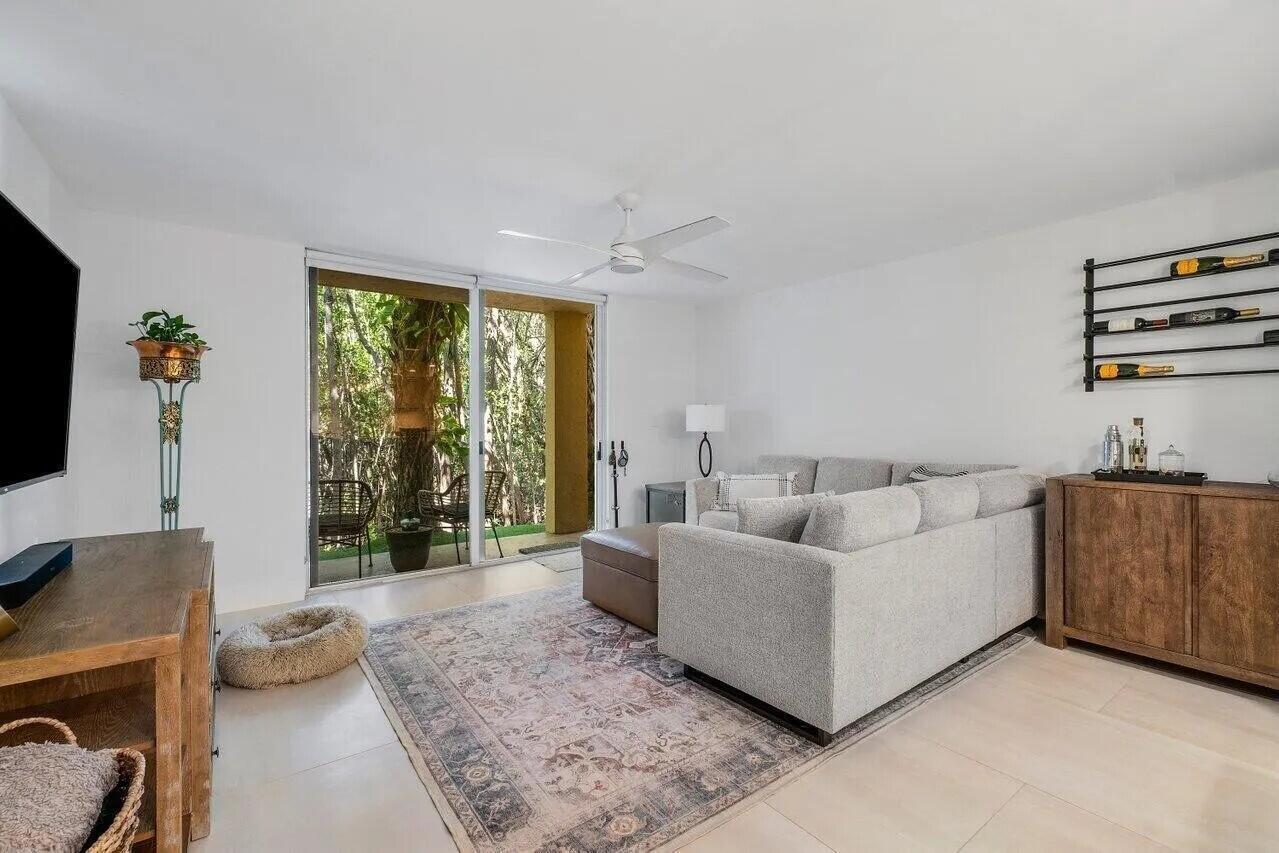 A living room features a grey sectional sofa, a patterned rug, and a sliding glass door — 1100 Scotia Drive # 105, Hypoluxo FL 33462, HYPOLUXO, FL