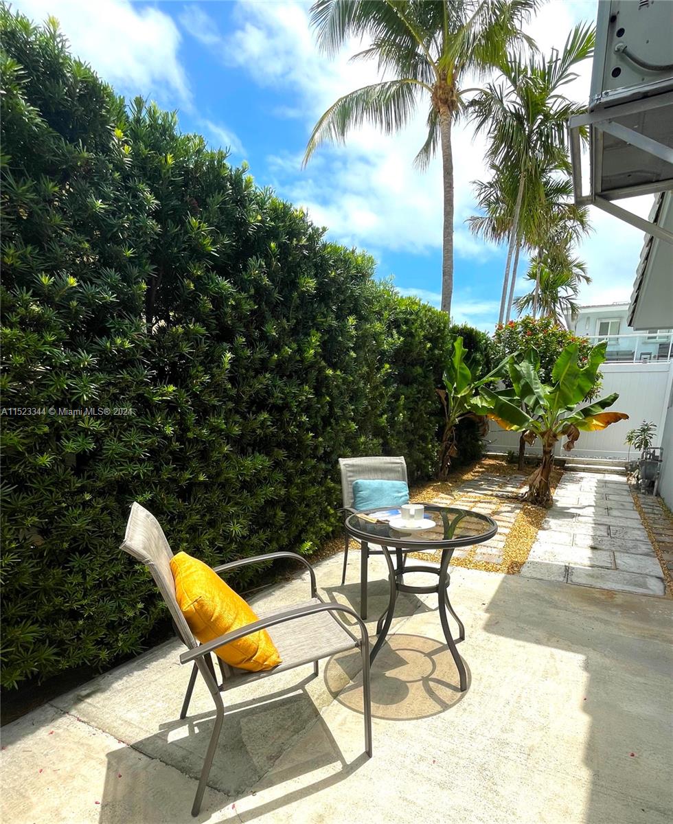 A small patio features a glass-topped table, two chairs, and a tall privacy hedge — 331 Desoto St, Hollywood FL 33019, HOLLYWOOD, FL