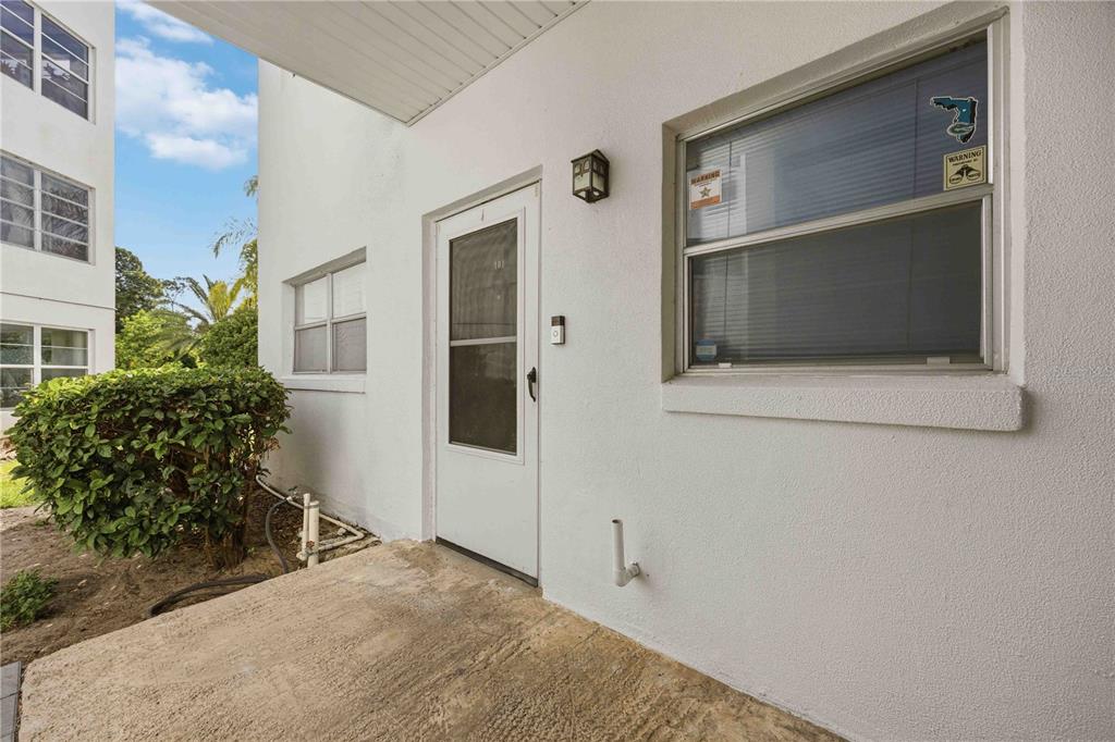 A white exterior wall features a front door, a window, and a concrete porch — 100 EL CAMINO DRIVE UNIT 101, WINTER HAVEN, FL