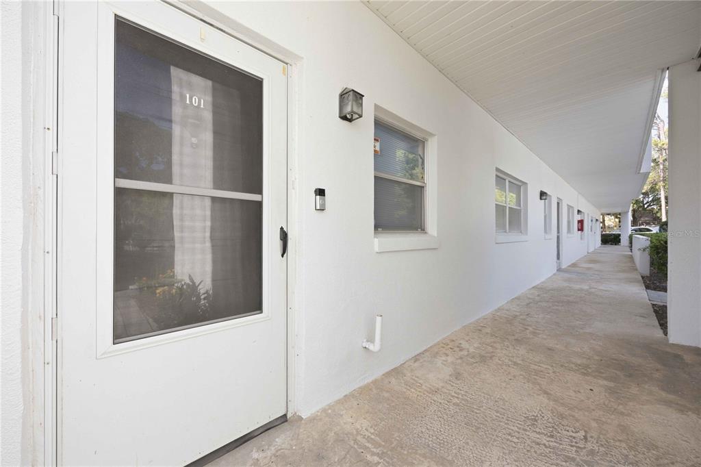 An exterior view of a white apartment building with a concrete walkway and unit 101 — 100 EL CAMINO DRIVE UNIT 101, WINTER HAVEN, FL