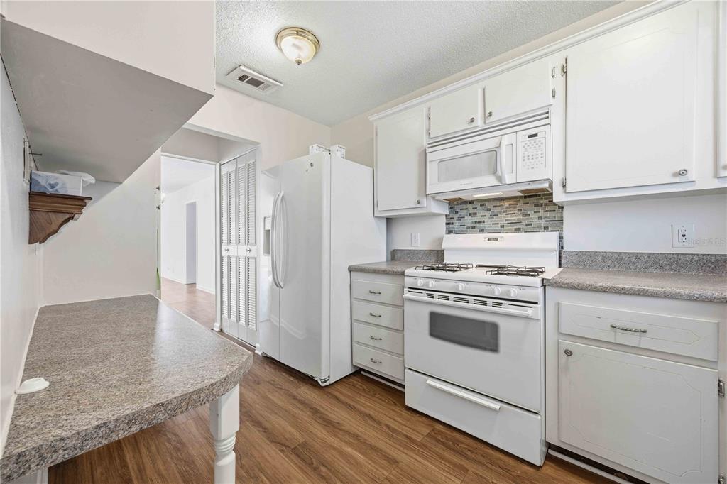 A kitchen with white cabinets, a gas stove, a white refrigerator, and wood-look flooring — 100 EL CAMINO DRIVE UNIT 101, WINTER HAVEN, FL