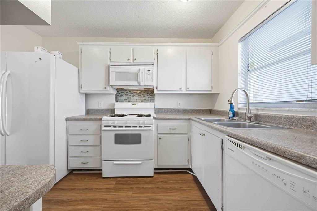 A kitchen with white cabinets, white appliances, a tiled backsplash, and wood-look flooring — 100 EL CAMINO DRIVE UNIT 101, WINTER HAVEN, FL