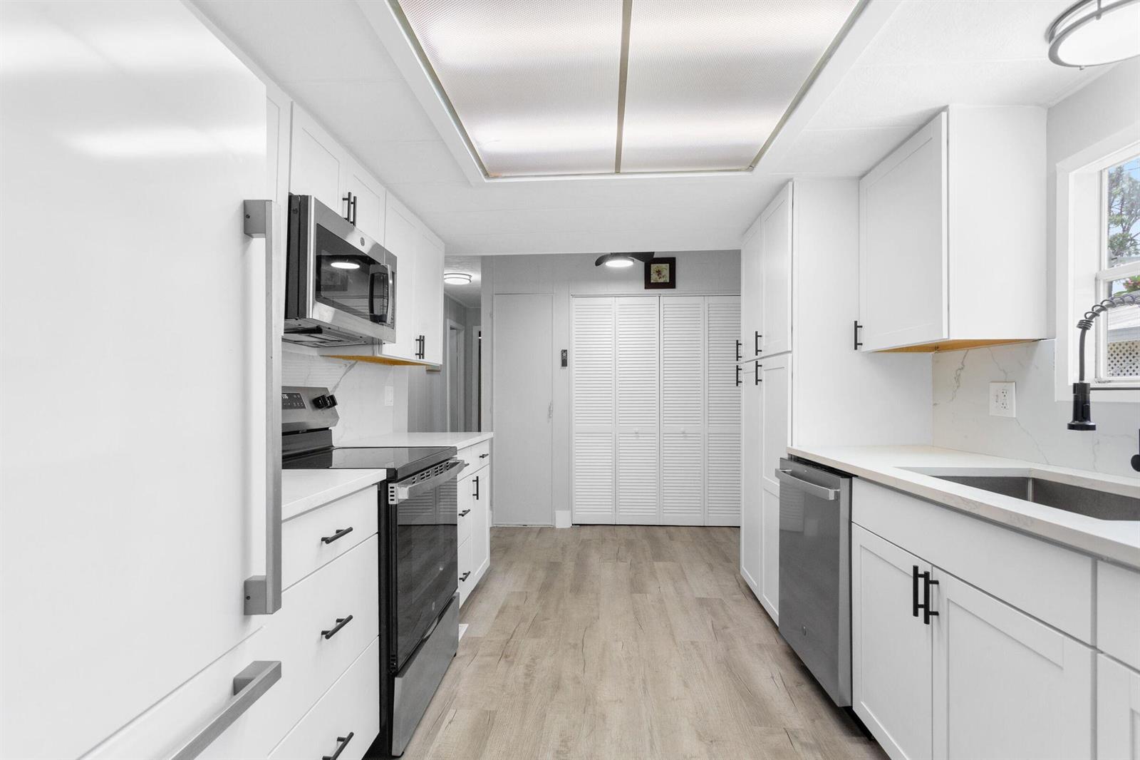 A modern galley kitchen features white cabinets, stainless steel appliances, and light wood-look flooring — 3008 Bimini Bay, Boynton Beach FL 33436, BOYNTON BEACH, FL