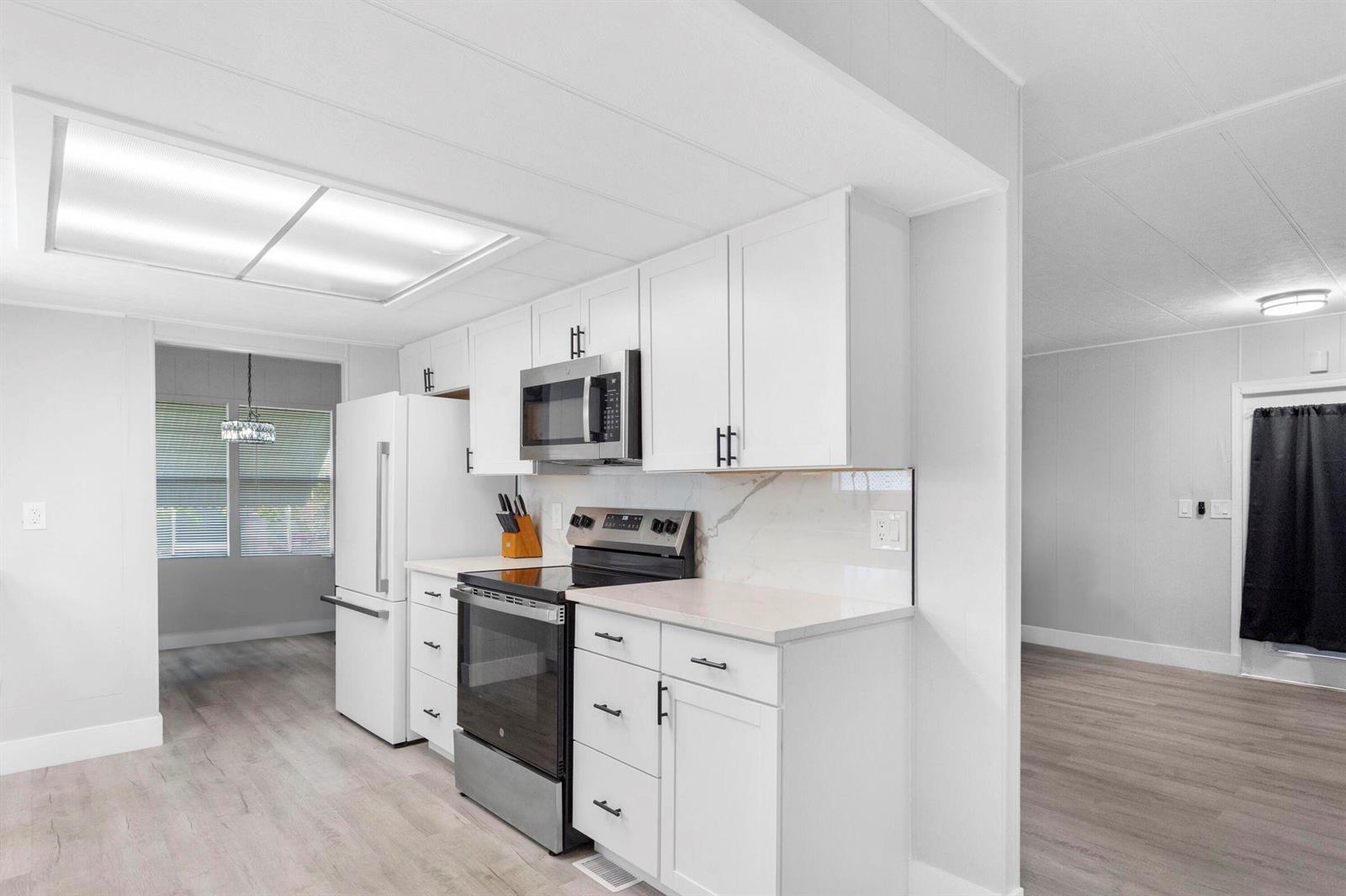 A modern kitchen features white cabinets, stainless steel appliances, and light wood-look flooring — 3008 Bimini Bay, Boynton Beach FL 33436, BOYNTON BEACH, FL