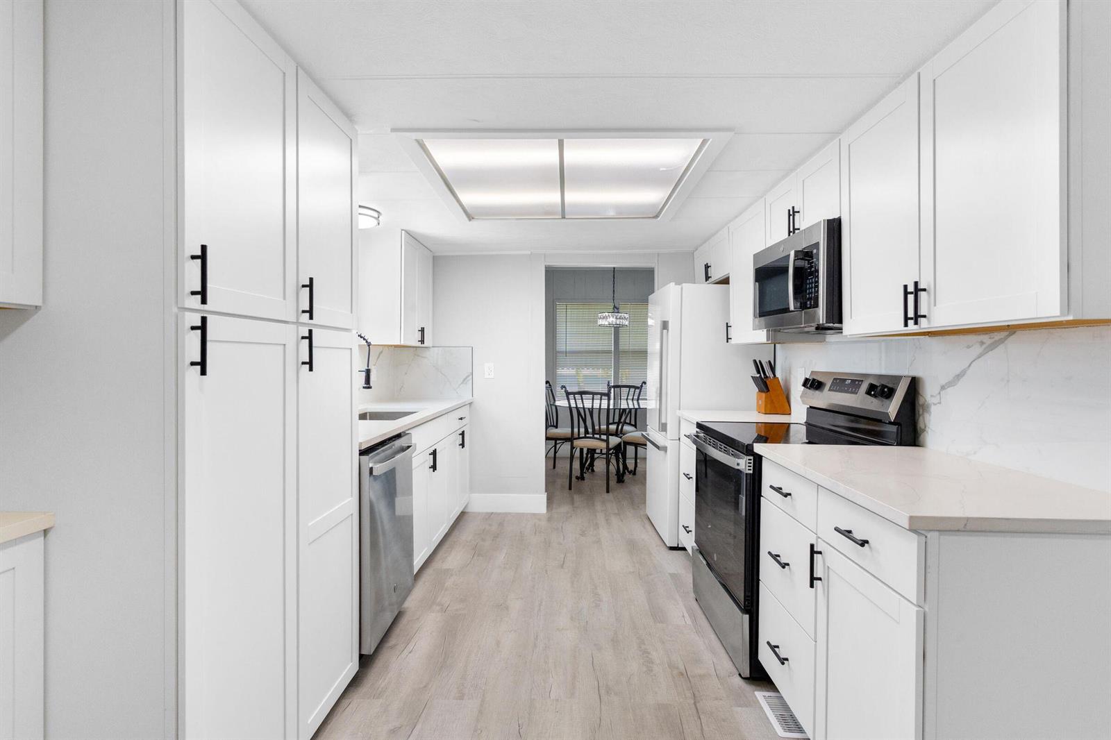 A galley kitchen features white cabinets, stainless steel appliances, and light wood-look flooring — 3008 Bimini Bay, Boynton Beach FL 33436, BOYNTON BEACH, FL