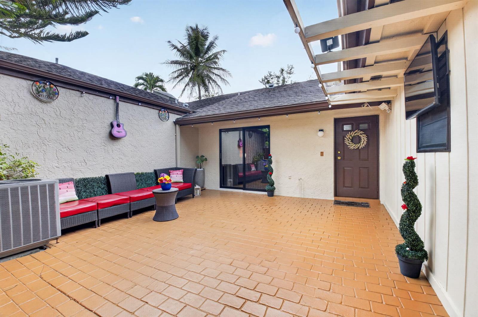 A paved outdoor patio features a seating area, a brown door, and a sliding glass door — 22602 Vistawood Way, Boca Raton FL 33428, BOCA RATON, FL