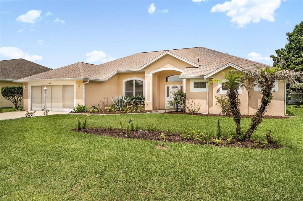 A single-story tan house with a two-car garage and a landscaped front yard — 3 WALLA PLACE, PALM COAST, FL