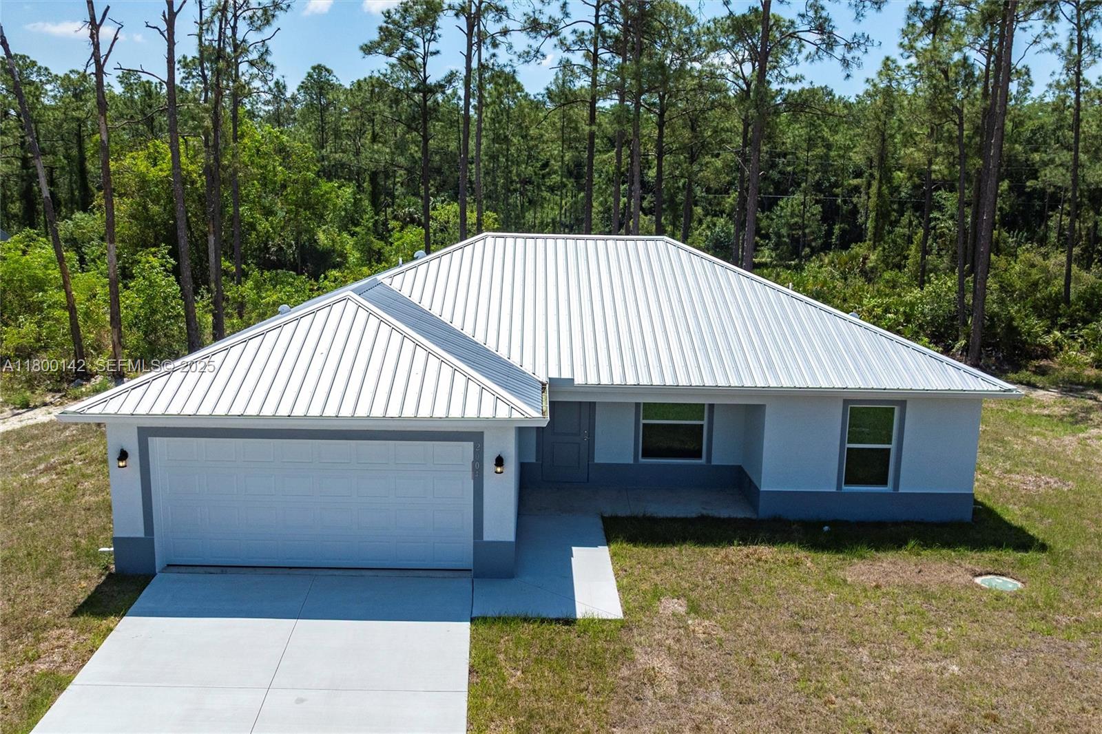 An aerial view of a single-story house with a metal roof and attached garage — 2004 Rosa Ct, Lehigh Acres FL 33972, LEHIGH ACRES, FL