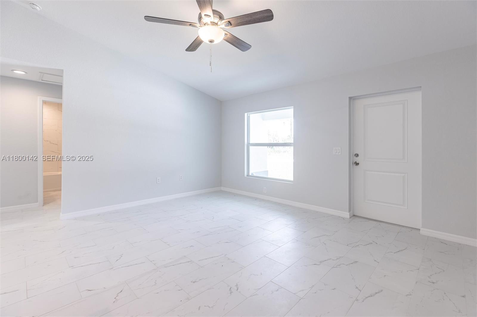 A bright, empty room features light gray walls, white marble-look tile flooring, and a ceiling fan — 2004 Rosa Ct, Lehigh Acres FL 33972, LEHIGH ACRES, FL