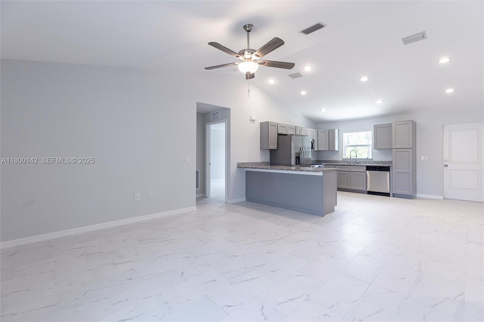 A kitchen with grey cabinets and a breakfast bar opens into a large tiled room — 2004 Rosa Ct, Lehigh Acres FL 33972, LEHIGH ACRES, FL