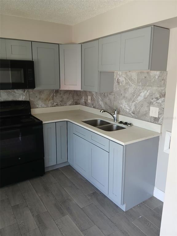 A kitchen features gray shaker cabinets, a black stove, a stainless sink, and marble-look backsplash — 38939 NORTH AVENUE UNIT 2, ZEPHYRHILLS, FL