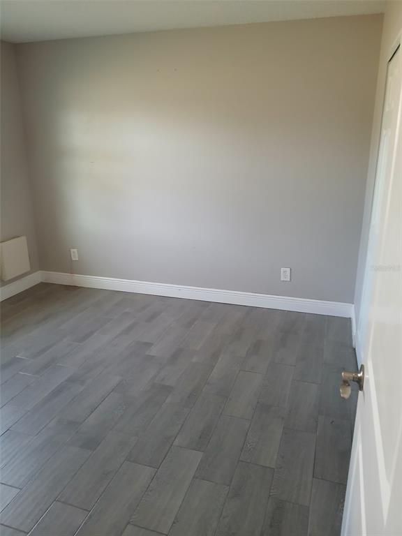 An empty bedroom features gray walls, white baseboards, and dark wood-look flooring — 38939 NORTH AVENUE UNIT 2, ZEPHYRHILLS, FL