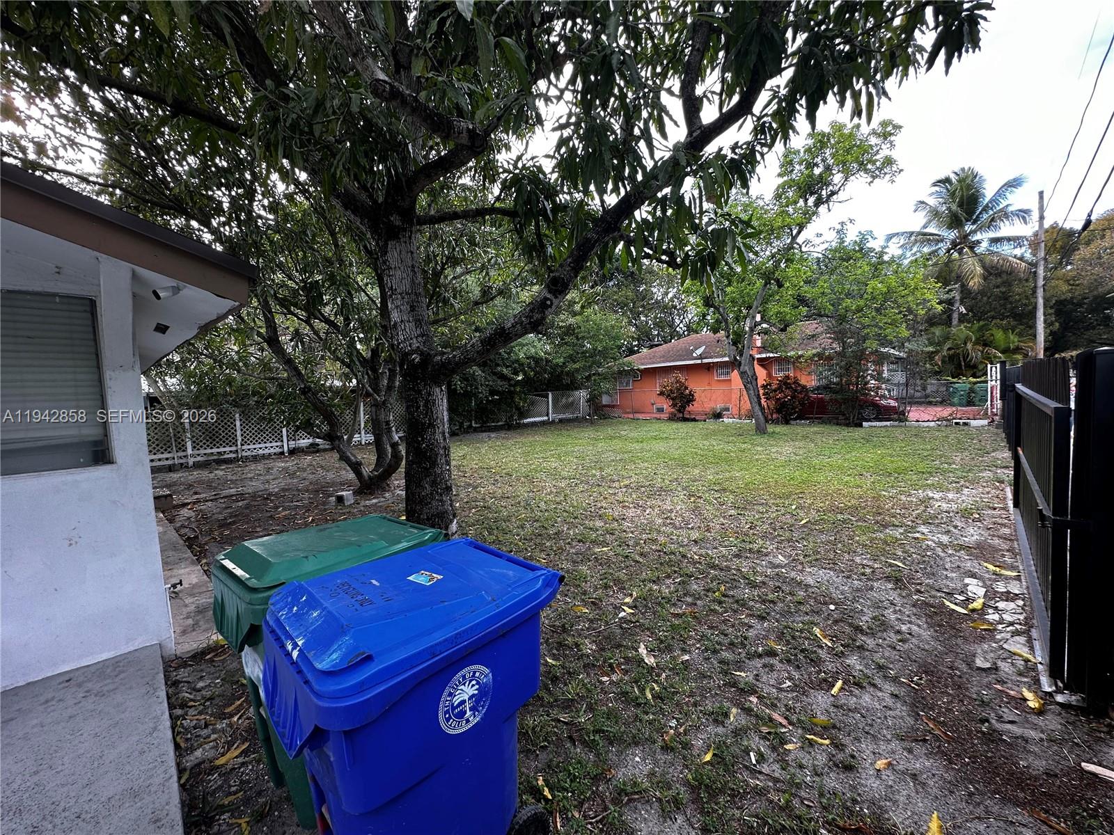 A backyard features a grassy lawn, mature trees, two trash bins, and a neighboring house — 105 NW 31st St # 1, Miami FL 33127, MIAMI, FL